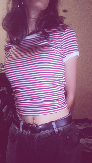 Buxom brunette in striped crop top and jeans in bedroom.
