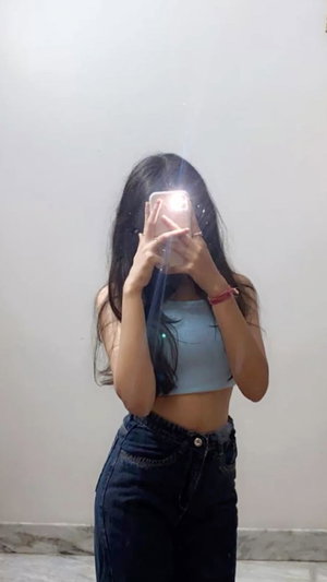 Slim woman with black hair in blue crop top and jeans, mirror selfie.