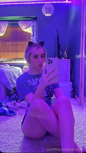 Woman in casual t-shirt and shorts takes mirror selfie in bedroom with purple lighting.