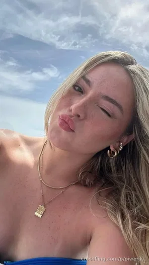 Woman with blonde hair, freckles, and gold jewelry posing outdoors in a blue top.