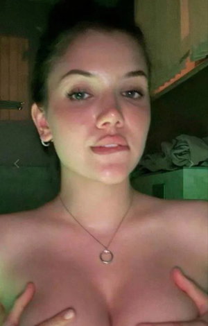 Dark-haired woman taking a topless selfie indoors.