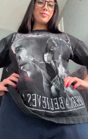 Woman with glasses and dark hair wearing graphic t-shirt indoors.