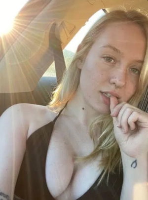 Blonde woman in black top takes selfie in car.