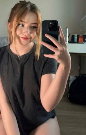 Woman with light brown hair taking a selfie in black t-shirt indoors.