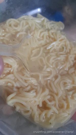 Close-up of cooked instant noodles in a clear container with a fork.