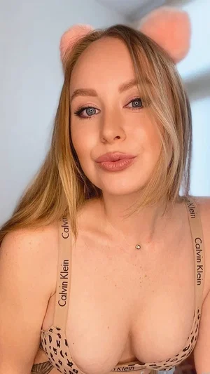 Woman with blonde hair wearing leopard print Calvin Klein bra and pink cat ears, indoor selfie.