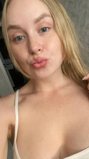 Blonde woman in white top making a playful face indoors.