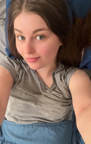 Woman with brown hair in gray shirt lying on bed.