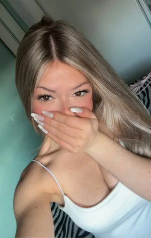 Blonde woman in white tank top taking selfie indoors.