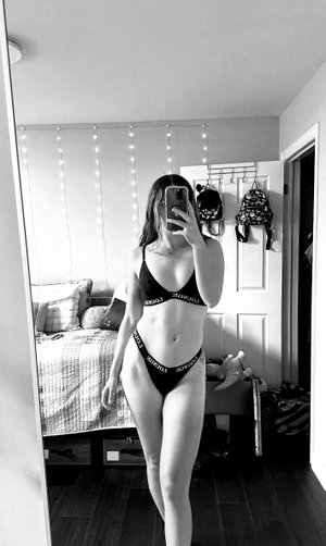 Fit woman in black bra and thong in bedroom mirror selfie.
