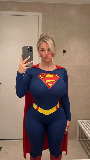 Woman in Superman costume taking mirror selfie in tiled room.