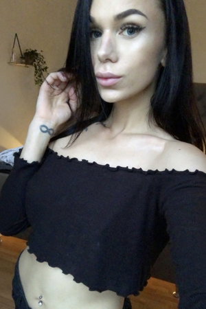 Woman with long dark hair in black off-shoulder top indoors.