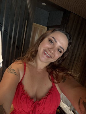Smiling woman with brown hair in red top taking indoor selfie.