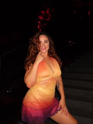 Curvy woman in gradient dress posing on dark stairs.