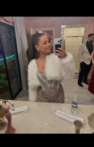 Woman in fur jacket and sequin dress in bathroom mirror selfie.