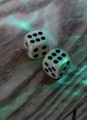 Two white dice with black dots on a wooden surface under green lighting.