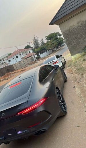 Two luxury cars parked on a dirt road near a house, one black Mercedes GT 53.