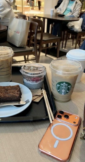 Table with Starbucks drinks, brownie, phone, and chopsticks in a cafe.
