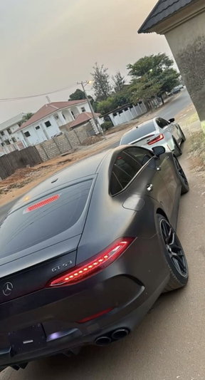 Two luxury cars parked on a residential street, one black Mercedes GTS with red taillights.