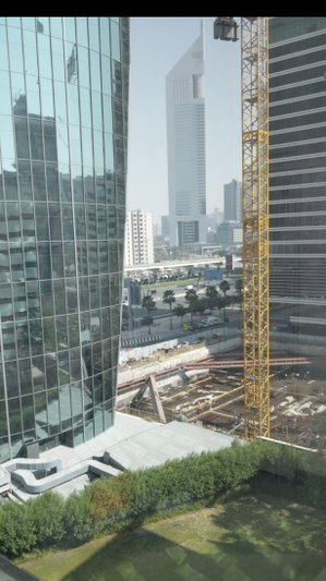 Cityscape with tall glass buildings, construction crane, and greenery in foreground.