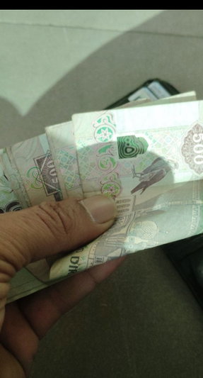 Hand holding a stack of 500 denomination banknotes indoors.