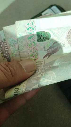 Hand holding a stack of currency bills with visible denominations and designs.