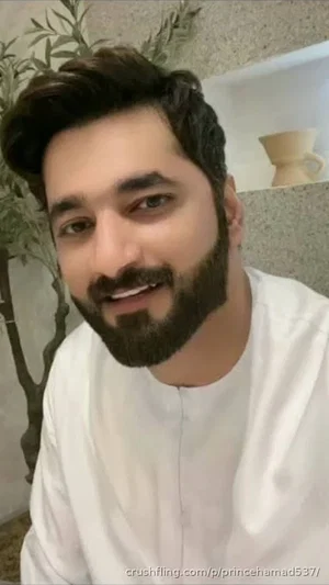 man with beard wearing white shirt, indoor setting with plant and shelf