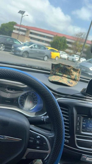 Car interior with camouflage hat on dashboard in parking lot.