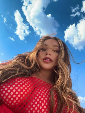 Woman with long wavy hair in red polka-dot top under blue sky.