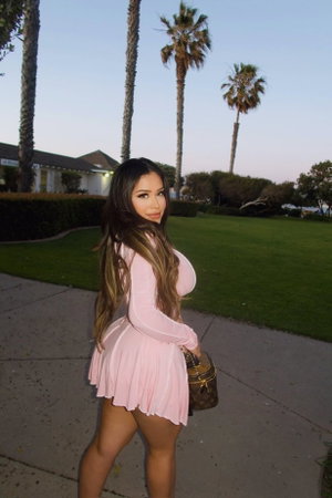 Woman in pink dress posing outdoors near palm trees and sidewalk.
