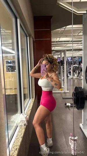 Woman in white crop top and pink shorts taking mirror selfie in gym.