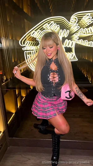 Woman with long blonde hair in a black corset top and pink plaid skirt posing in front of neon