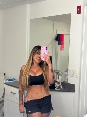 Blonde woman posing in bathroom mirror selfie with black crop top.