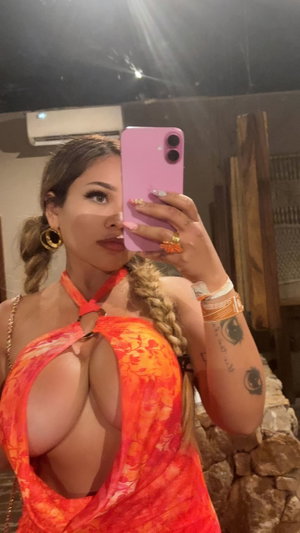 Woman with braided hair taking mirror selfie in orange dress.
