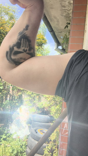 Man with large arm tattoo wearing black shirt outdoors.