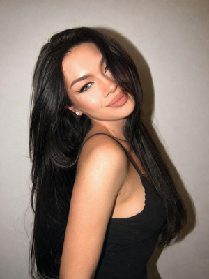 Woman with long black hair in black top posing indoors.