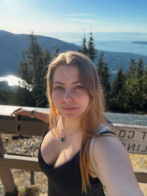 Blonde woman in black top taking selfie at mountain overlook.