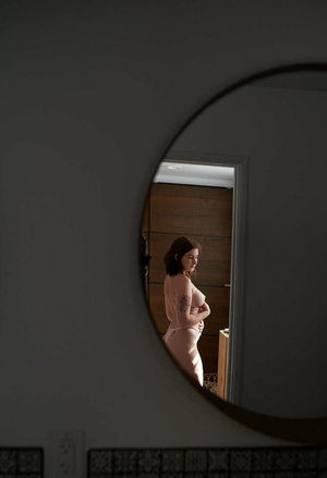 Woman with tattoos in pink underwear seen in round mirror.