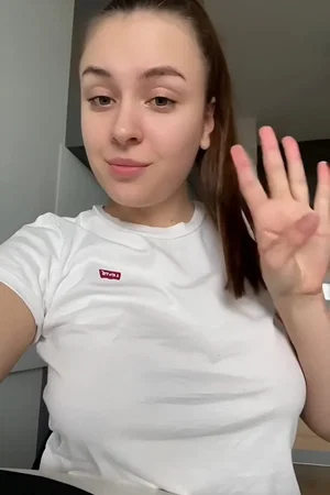 Woman in white t-shirt waving, indoor setting, casual pose.