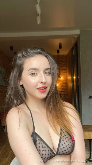 Woman with long hair in sheer heart-patterned bra, indoors in a warmly lit room.