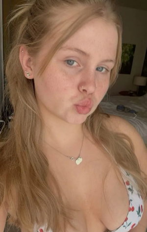 Blonde woman in cherry top taking bedroom selfie.