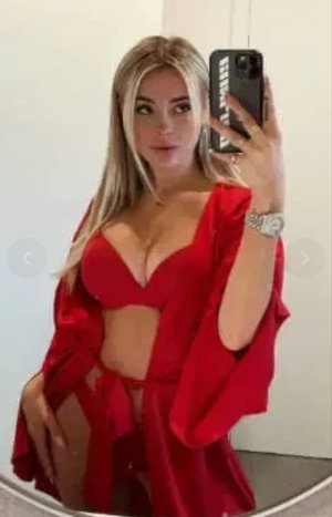 Blonde woman in red lingerie taking mirror selfie indoors.