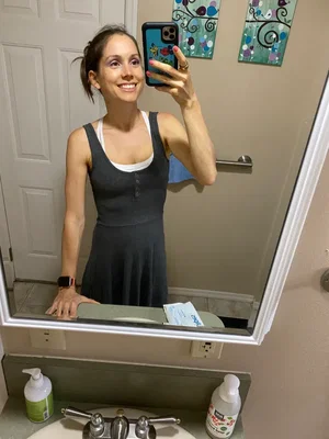 Woman in gray dress taking bathroom mirror selfie.
