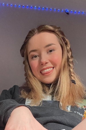 Blonde woman with braids in hoodie taking indoor selfie.