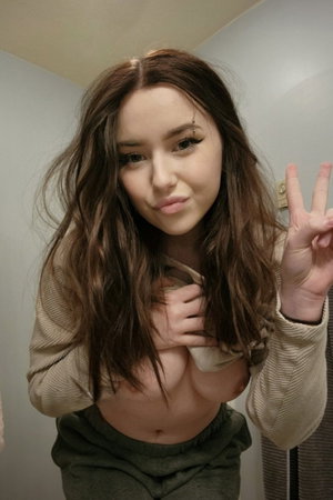 Woman with long brown hair posing in mirror selfie indoors.