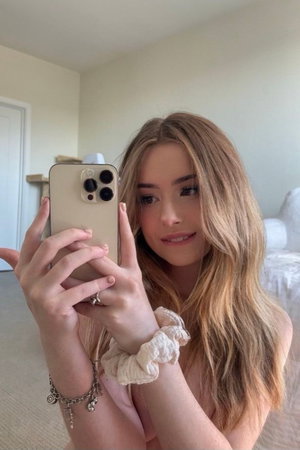 Blonde woman taking a selfie in bedroom.