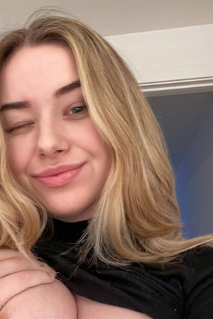 Blonde woman in black top winking in indoor selfie.