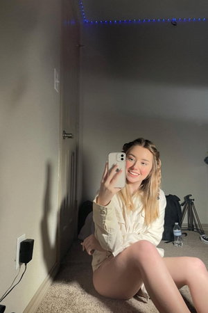 Woman with blonde hair in a light shirt sits on floor in room with blue string lights.