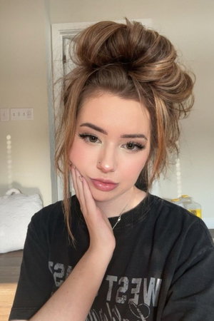 Woman with messy bun and makeup, wearing black t-shirt, posing indoors.