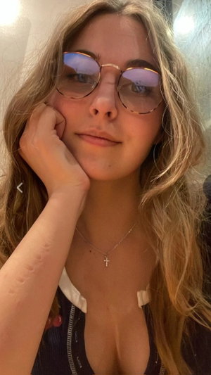 Blonde woman with glasses in low-cut top and necklace indoors.